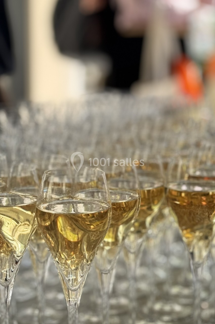 Rangée de verres à pied remplis de vin blanc pétillant, disposés sur une table lors d'un événement.