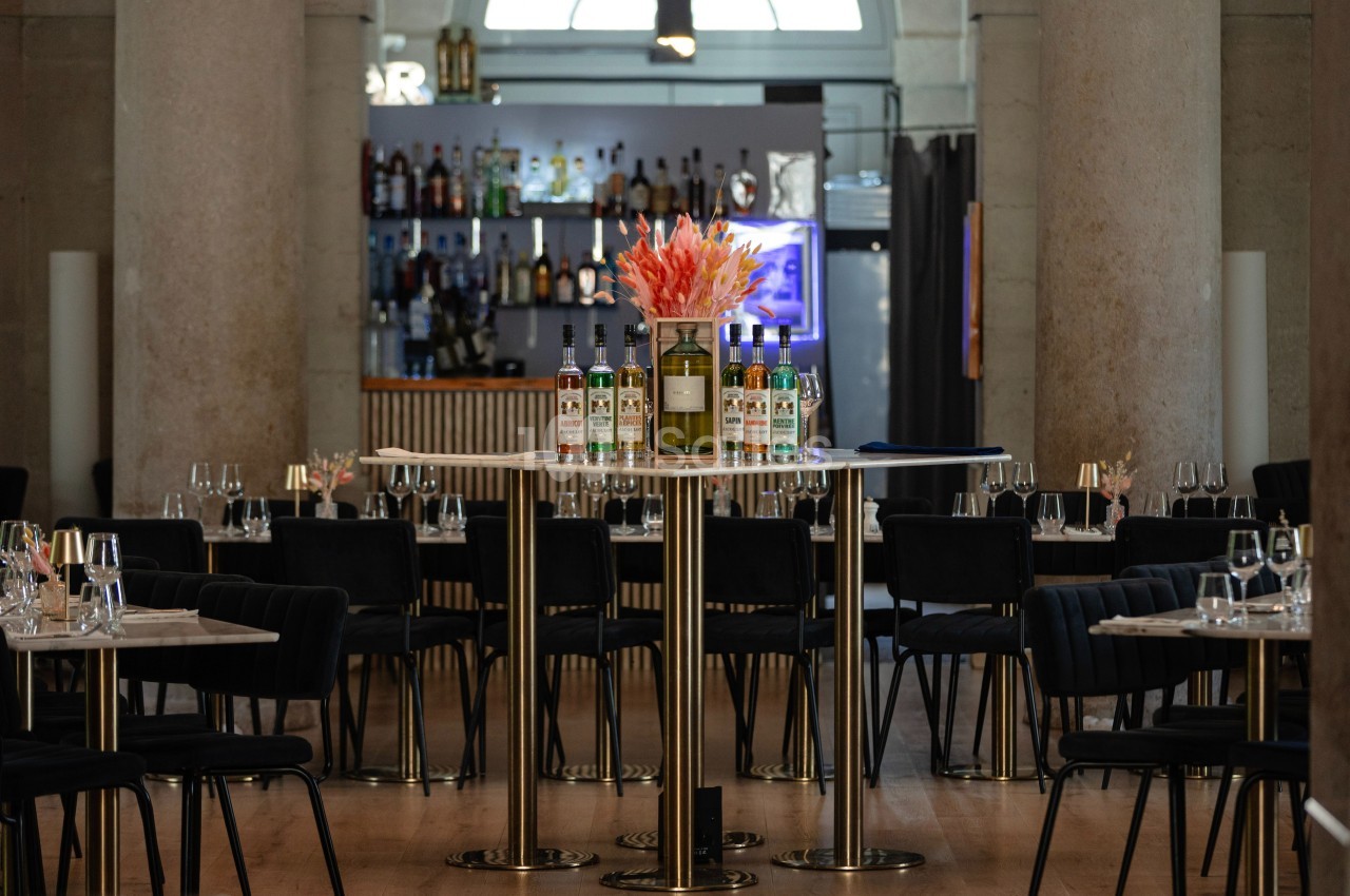 Salle de restaurant élégante avec tables dressées, bar en arrière-plan et fleurs au centre d'une table haute.