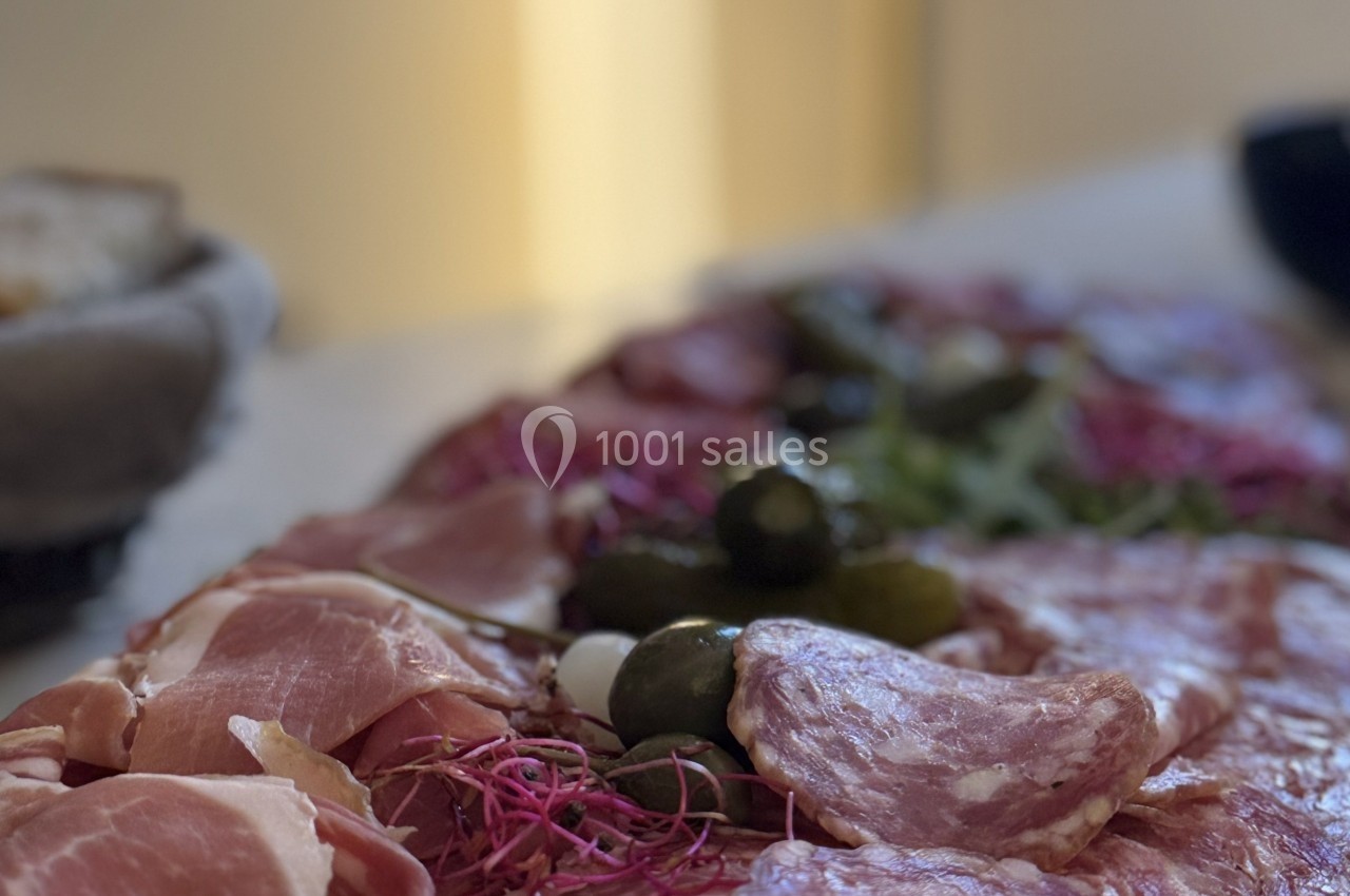 Plateau de charcuterie avec tranches de jambon, saucisson, cornichons et garniture végétale sur une table.