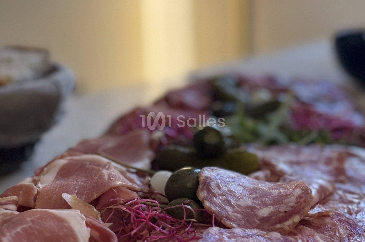 Plateau de charcuterie avec tranches de jambon, saucisson, cornichons et garniture végétale sur une table.