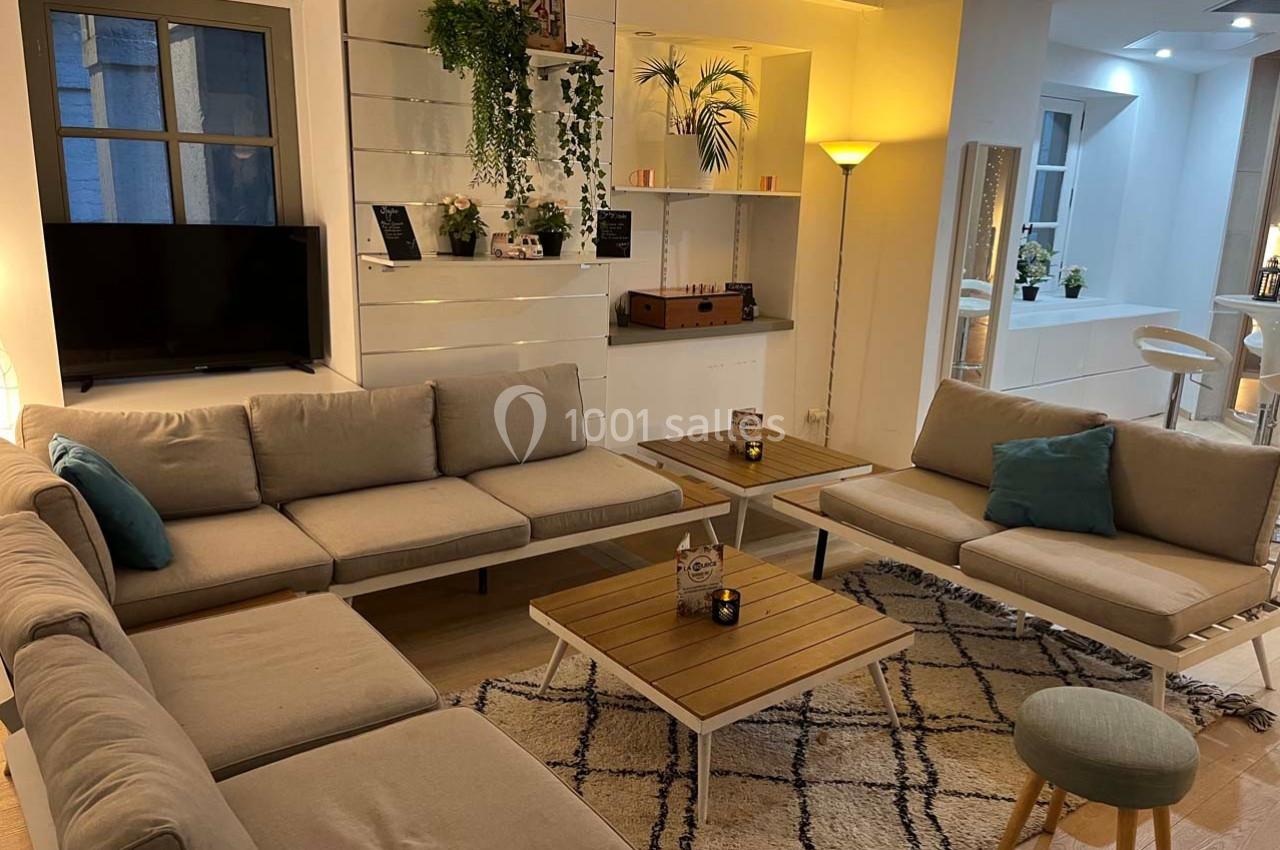 Salon moderne avec canapés beiges, tables basses en bois, plantes décoratives et éclairage chaleureux.