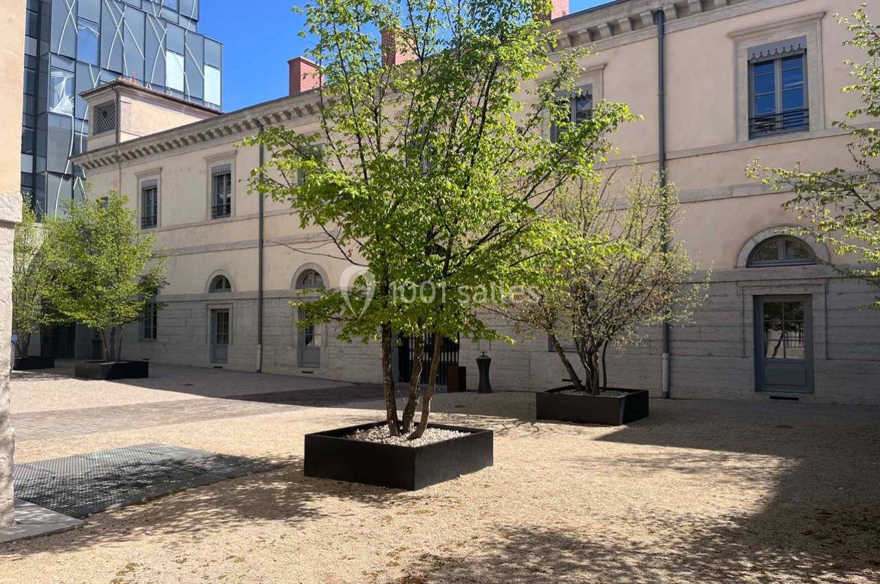 Cour intérieure avec des arbres en bacs, entourée de bâtiments en pierre et de façades modernes en arrière-plan.