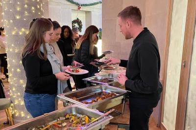 Groupe de personnes rassemblées autour de tables sous des parasols dans une cour extérieure avec végétation.