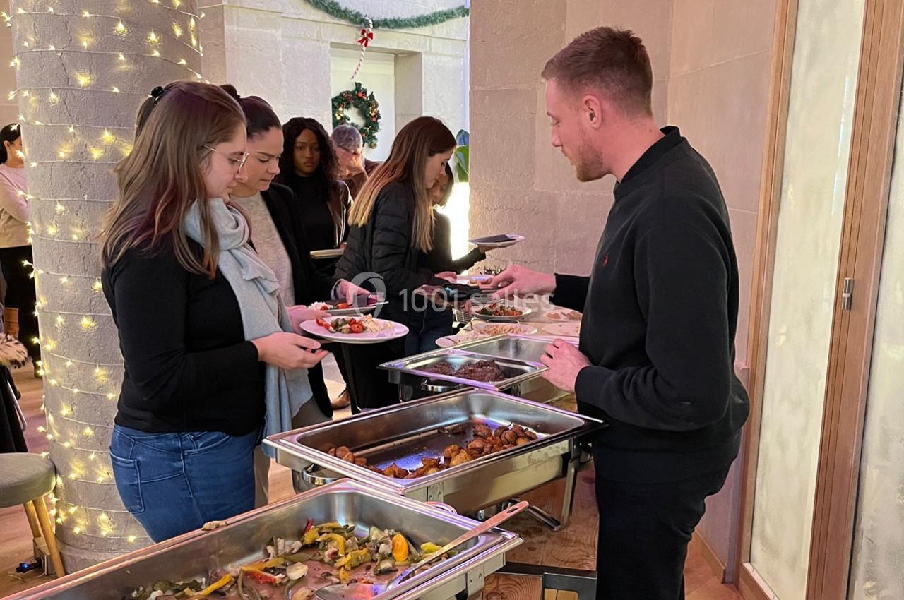 Des personnes se servent à un buffet chaud dans un espace décoré avec des lumières et une couronne de Noël.