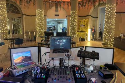 Groupe de personnes rassemblées autour de tables sous des parasols dans une cour extérieure avec végétation.