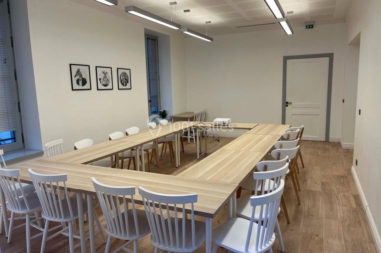 Salle de réunion lumineuse avec tables en bois disposées en U, chaises blanches et projecteur installé.