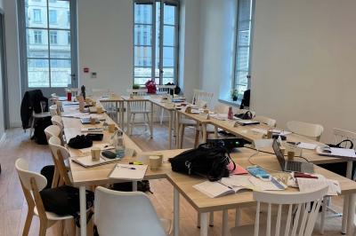 Groupe de personnes rassemblées autour de tables sous des parasols dans une cour extérieure avec végétation.