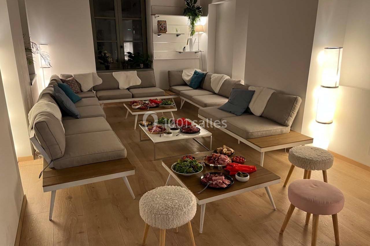 Salon moderne avec canapés beiges, tables basses garnies de plats variés et lumière tamisée.