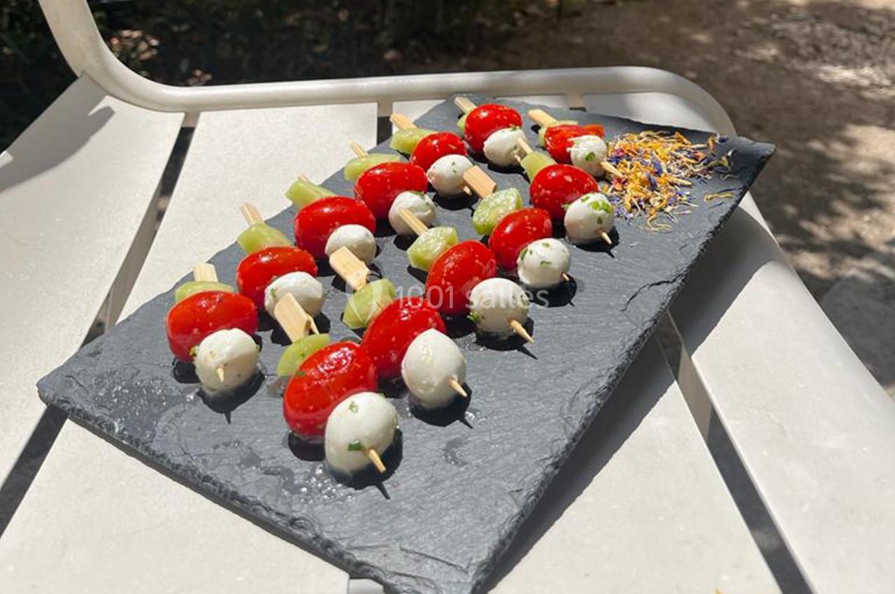 Brochettes apéritives avec tomates cerises, billes de mozzarella et morceaux de concombre sur une ardoise noire.
