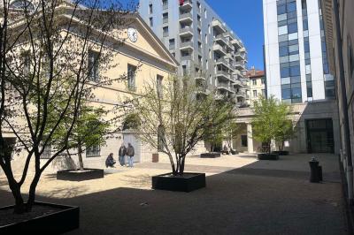 Groupe de personnes rassemblées autour de tables sous des parasols dans une cour extérieure avec végétation.