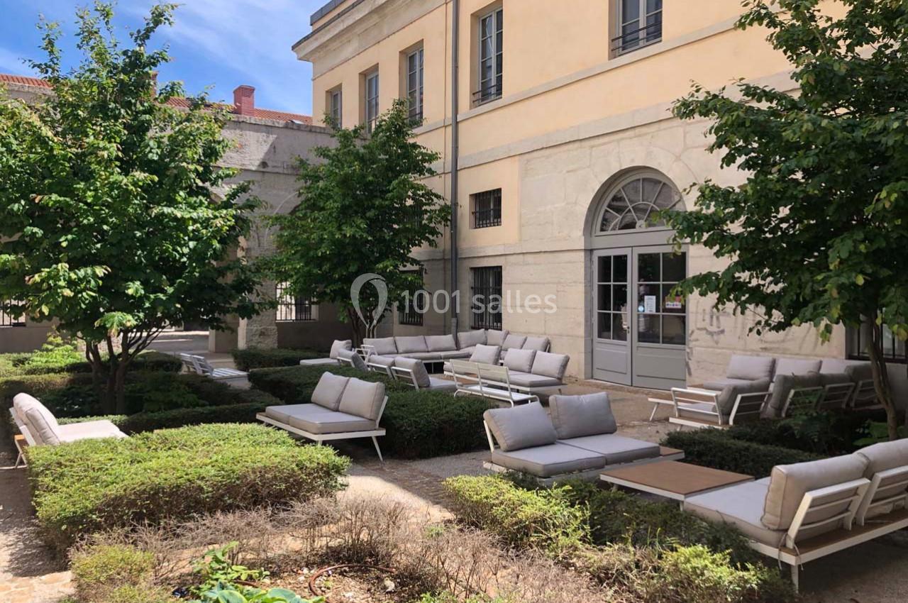 Cour intérieure avec mobilier de jardin moderne, entourée de buissons taillés et d'arbres, près d'un bâtiment en pierre.