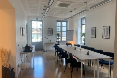 Groupe de personnes rassemblées autour de tables sous des parasols dans une cour extérieure avec végétation.