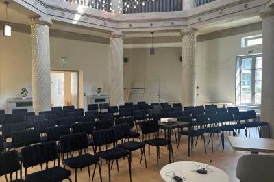 Groupe de personnes rassemblées autour de tables sous des parasols dans une cour extérieure avec végétation.