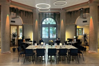 Groupe de personnes rassemblées autour de tables sous des parasols dans une cour extérieure avec végétation.