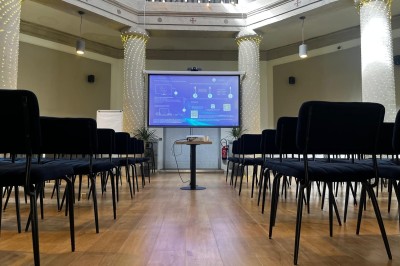 Groupe de personnes rassemblées autour de tables sous des parasols dans une cour extérieure avec végétation.