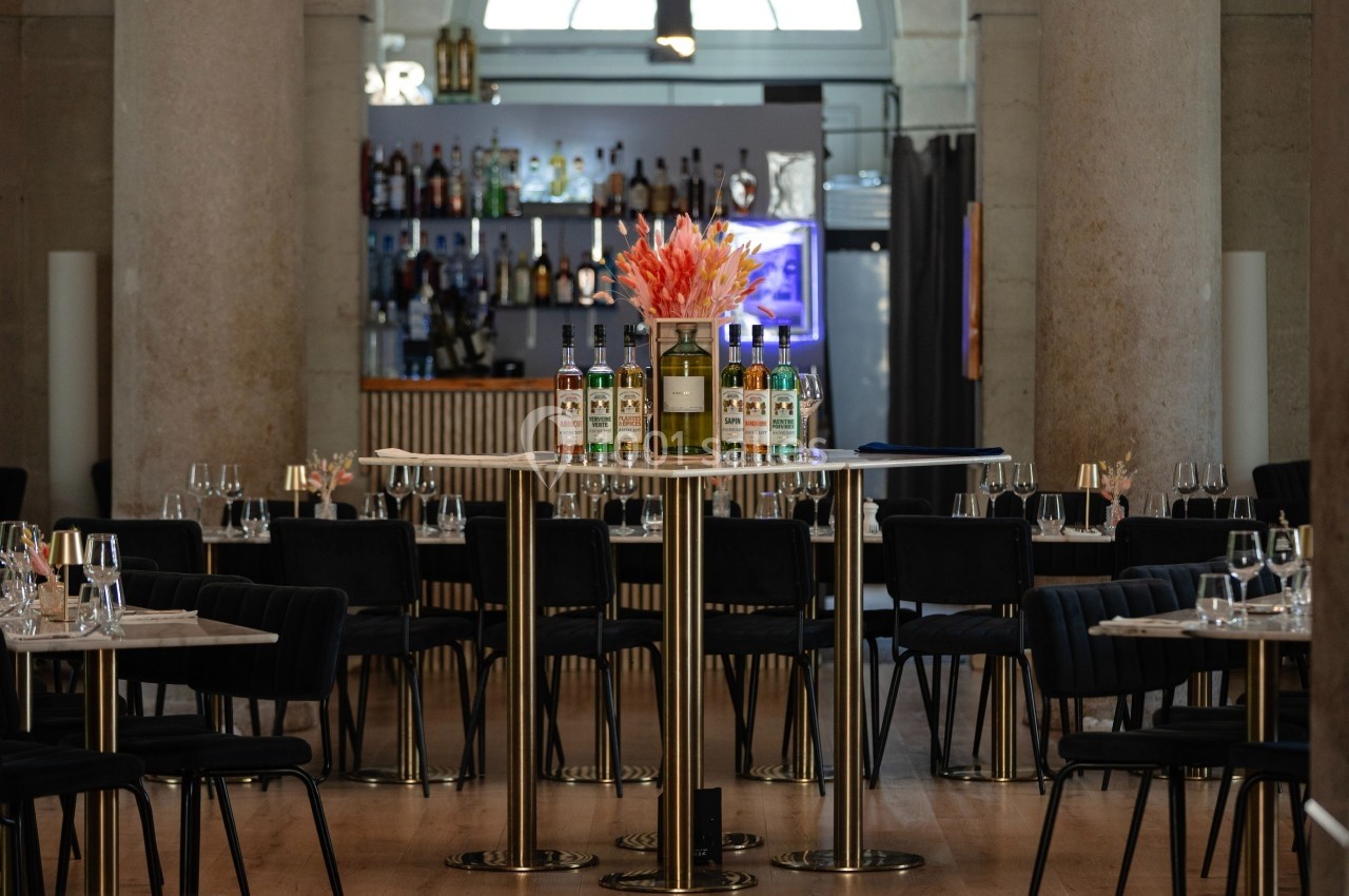 Salle de restaurant élégante avec tables dressées, bar en arrière-plan et fleurs au centre d'une table haute.