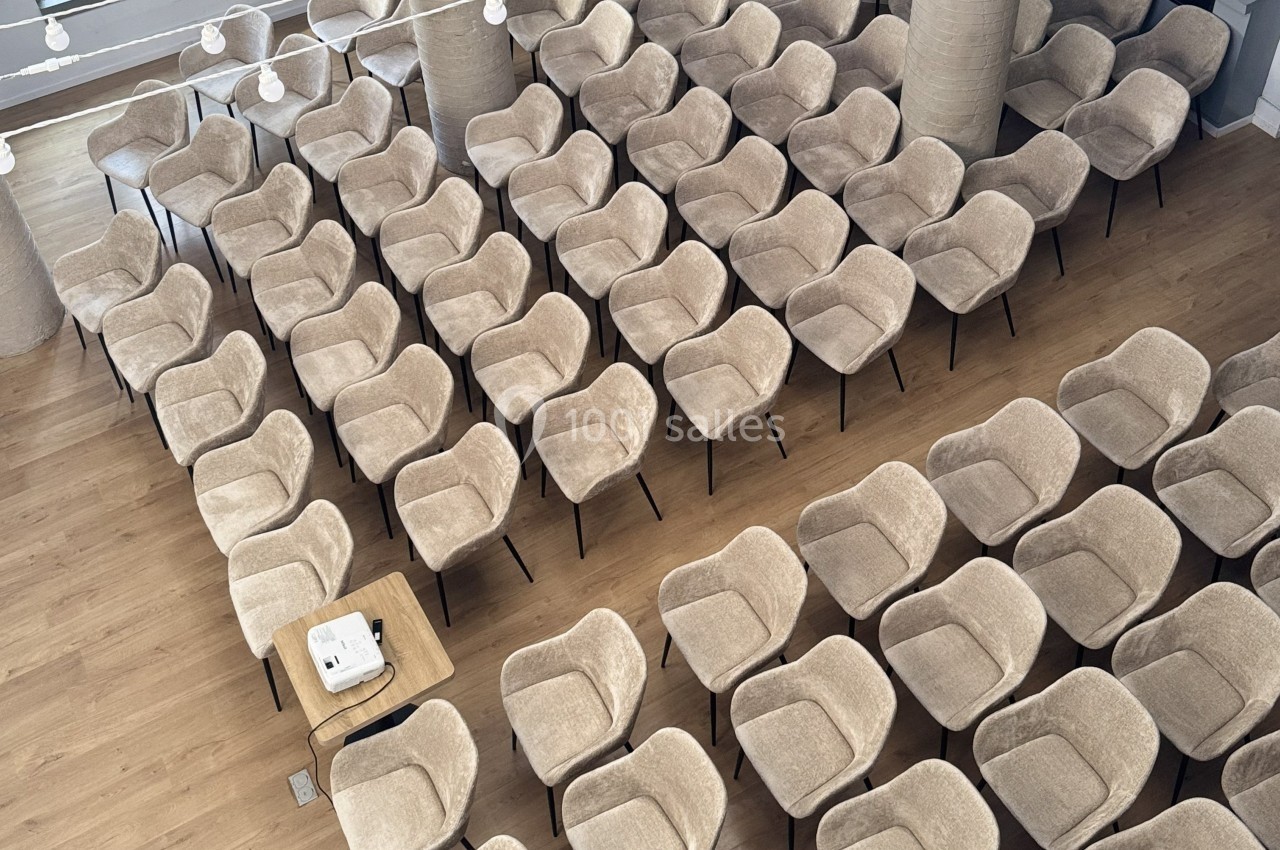 Salle avec des rangées de chaises beiges alignées, un projecteur posé sur une table au premier plan.