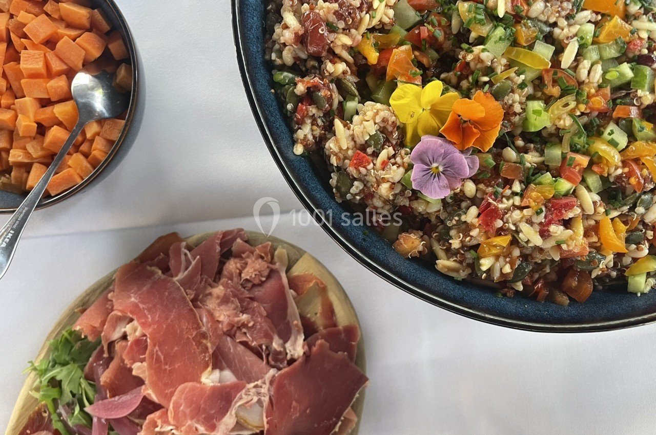 Salade colorée avec légumes et fleurs comestibles, accompagnée de cubes de patate douce et de tranches de jambon cru.