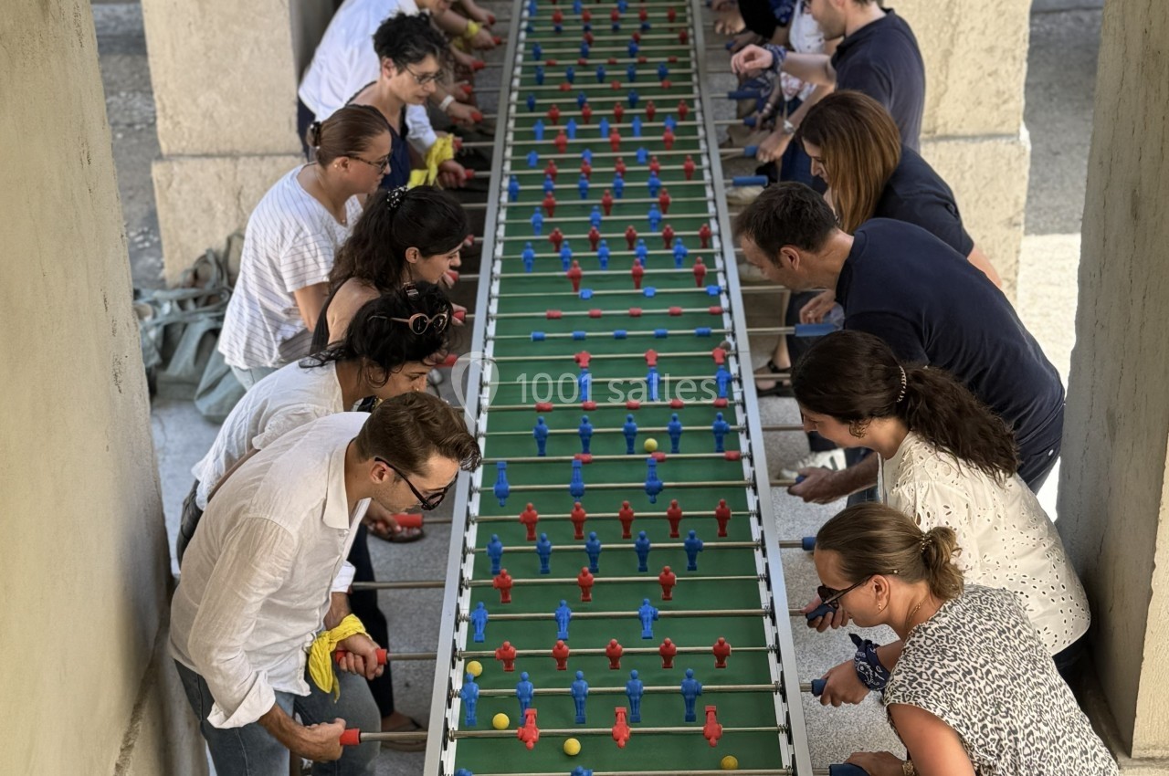 Des personnes jouent à un baby-foot géant avec plusieurs rangées de joueurs sous une structure en plein air.