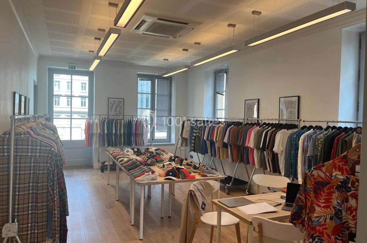 Salle lumineuse avec des vêtements suspendus sur des portants et des tables présentant des articles pliés.