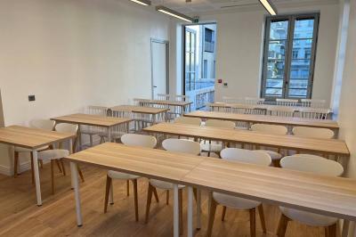 Groupe de personnes rassemblées autour de tables sous des parasols dans une cour extérieure avec végétation.