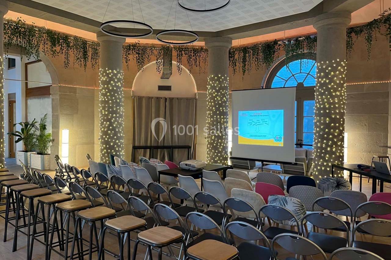 Salle de conférence décorée avec des guirlandes lumineuses, des chaises alignées et un écran de projection allumé.