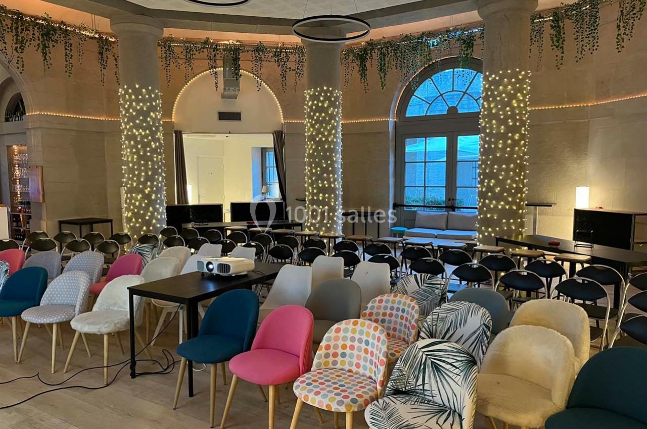 Salle de conférence décorée avec des guirlandes lumineuses, des chaises colorées et un projecteur installé à l'avant.