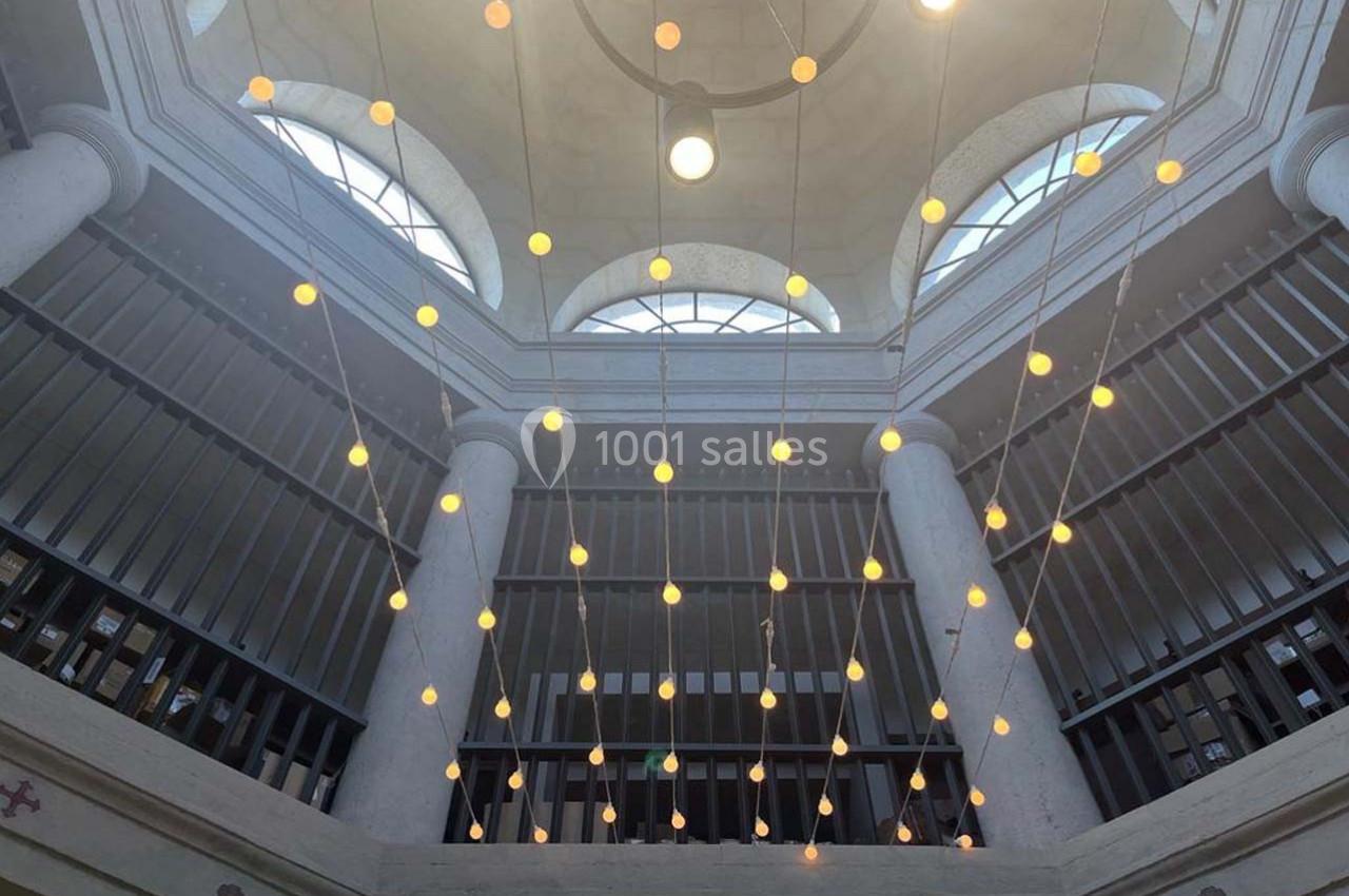 Plafond voûté avec des colonnes blanches et un éclairage suspendu composé de multiples ampoules rondes.