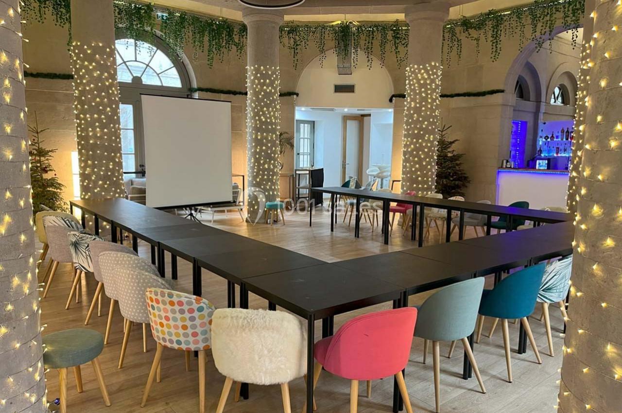 Salle de réunion lumineuse avec tables en U, chaises colorées et décorations lumineuses sur les colonnes.