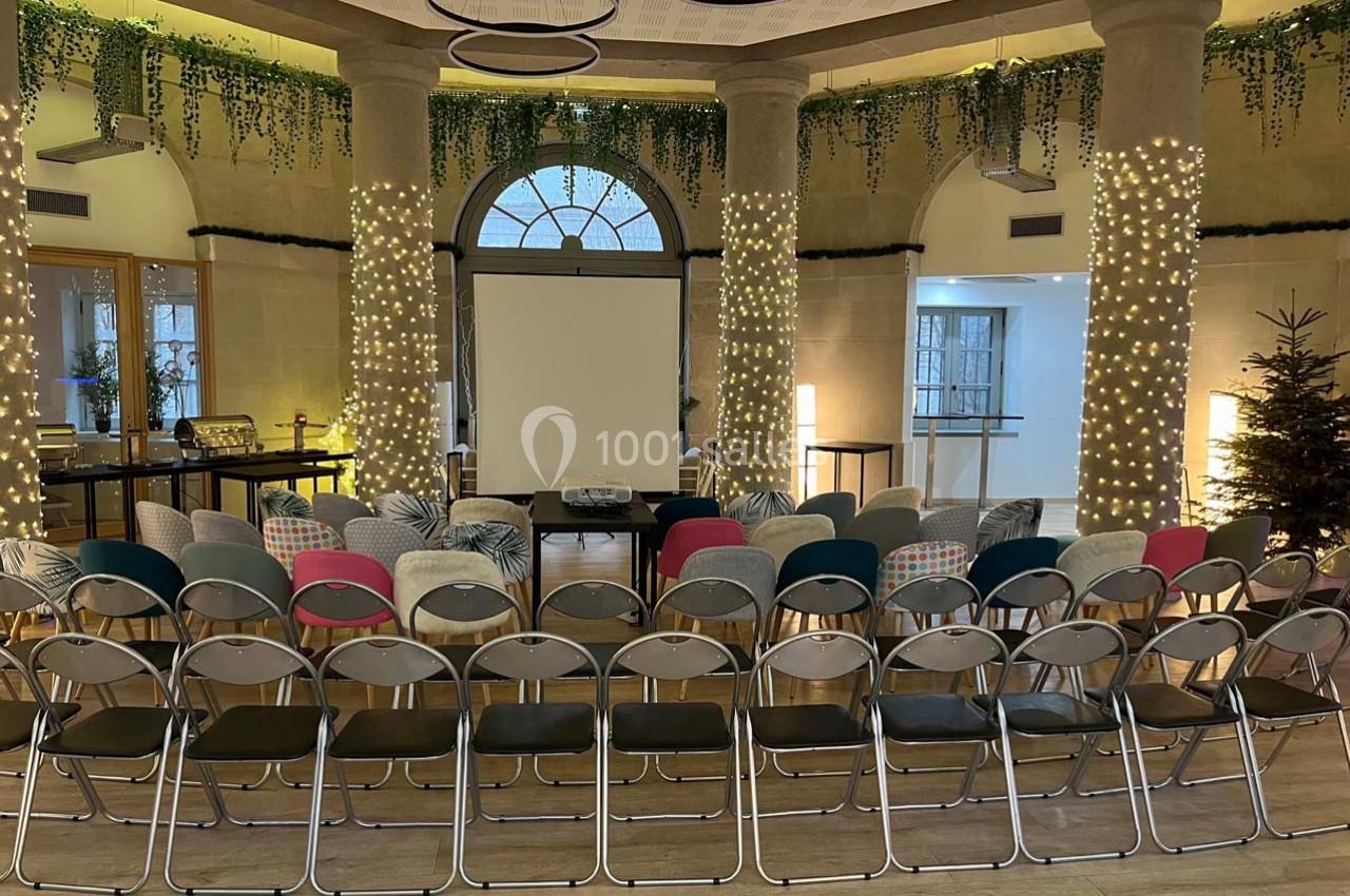 Salle de conférence décorée avec des guirlandes lumineuses, des chaises alignées face à un écran de projection.