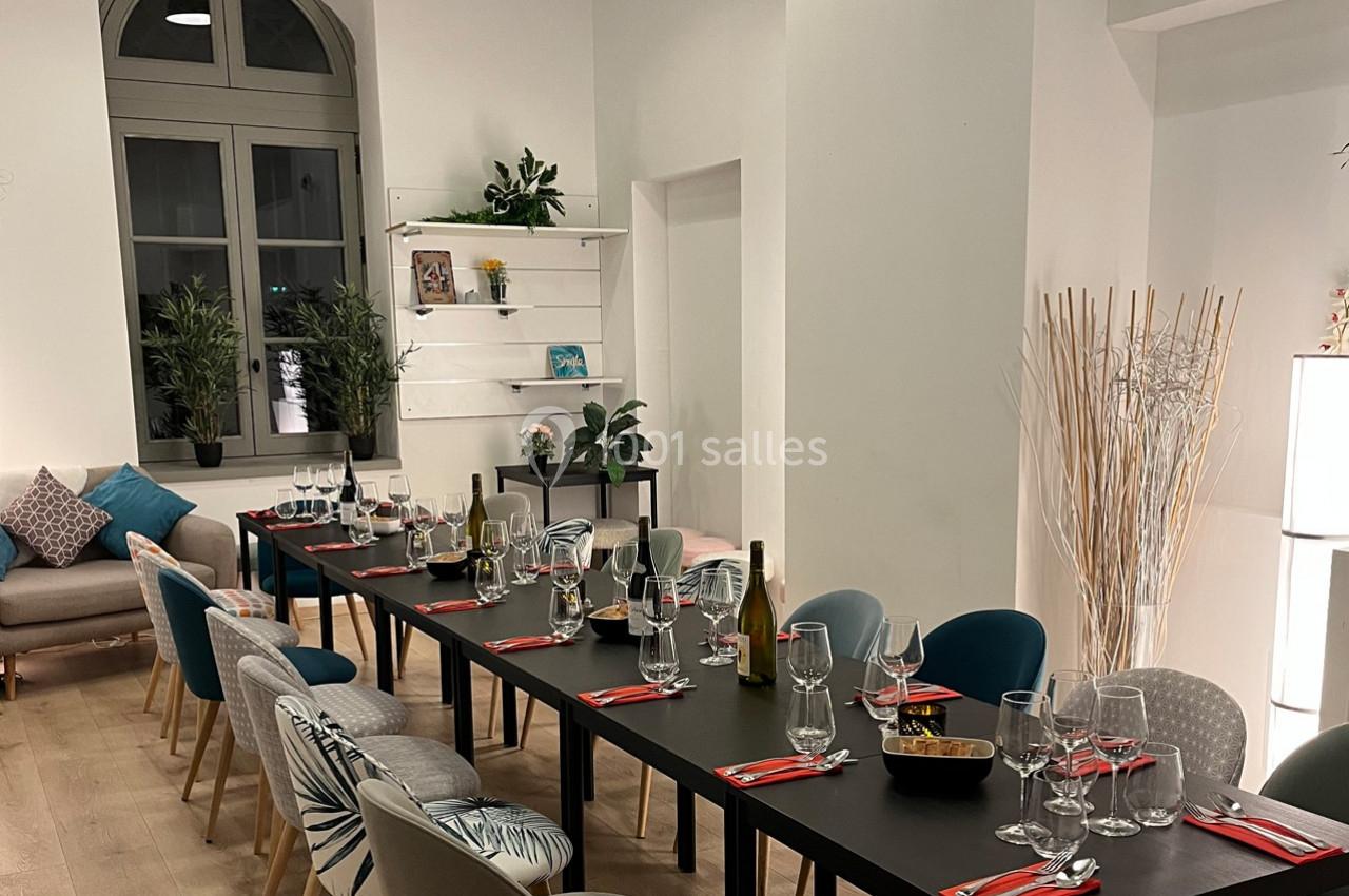 Salle lumineuse avec une grande table dressée, entourée de chaises colorées, décorée de plantes et d'étagères.
