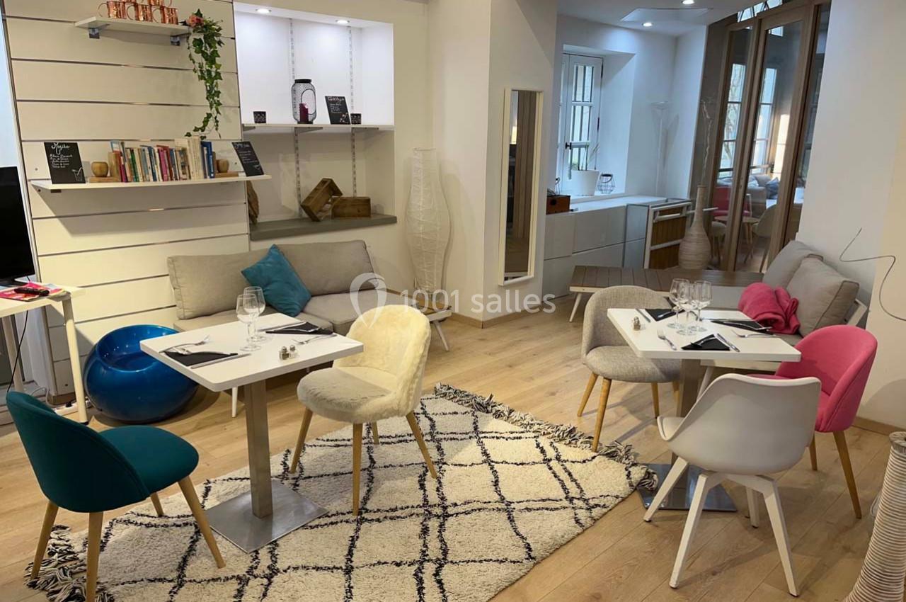 Espace intérieur lumineux avec tables dressées, chaises colorées, étagères décorées et tapis à motifs géométriques.