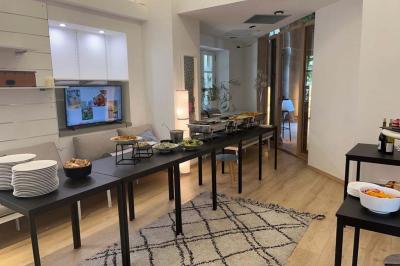 Groupe de personnes rassemblées autour de tables sous des parasols dans une cour extérieure avec végétation.