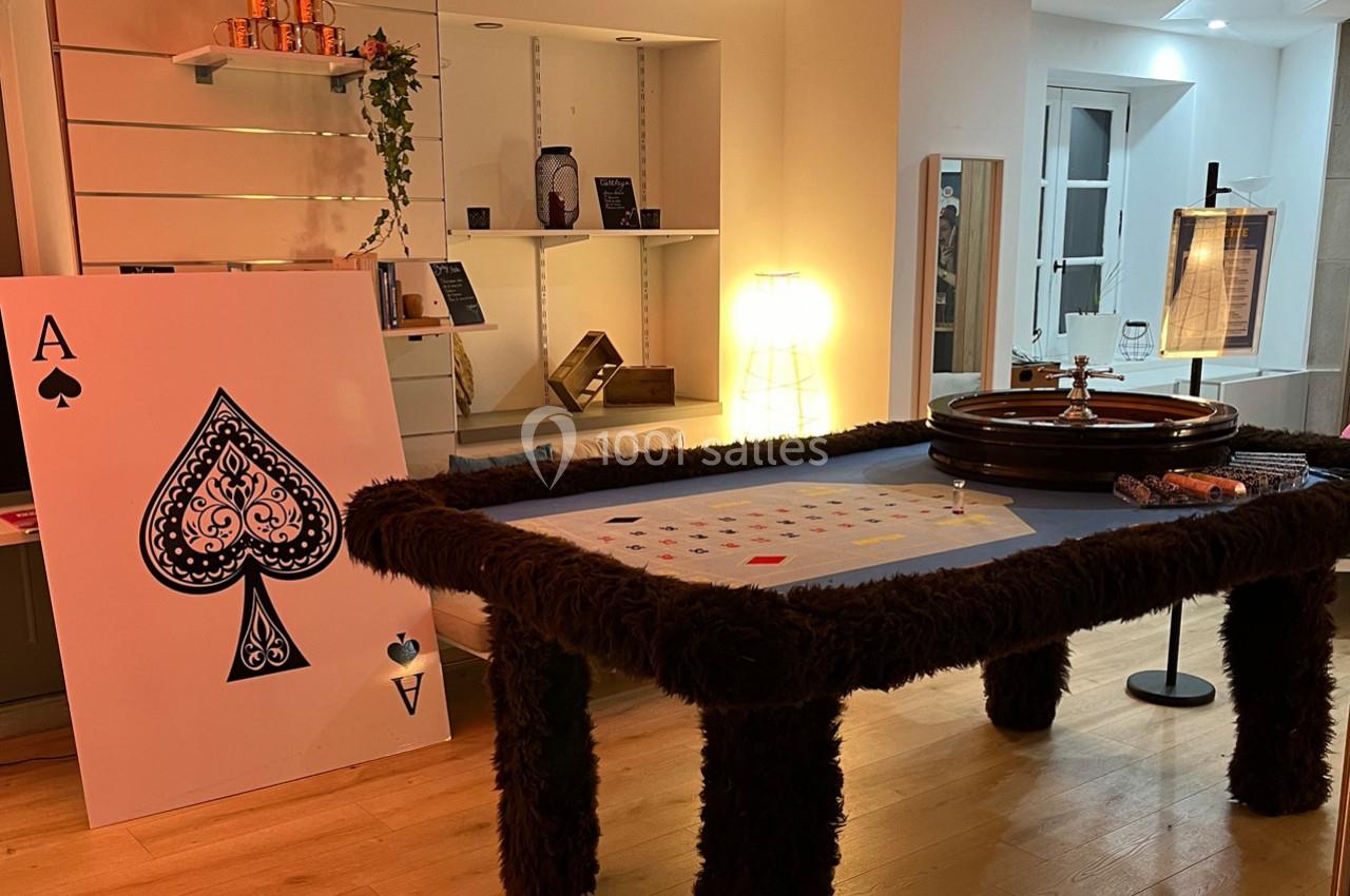 Table de jeu avec roulette, tapis de cartes et grande carte As de pique dans une pièce éclairée.