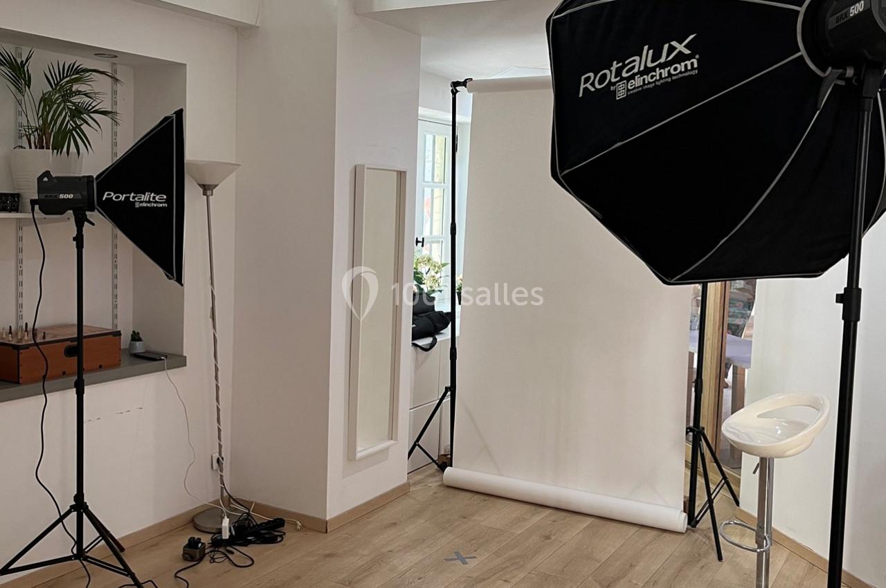 Studio photo avec éclairage professionnel, fond blanc déroulé et équipements installés dans une pièce lumineuse.