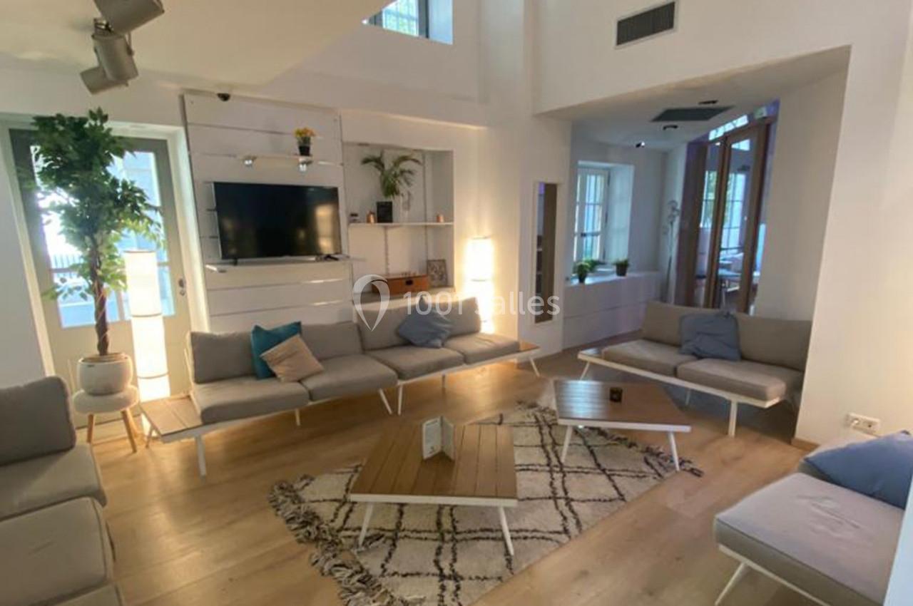 Salon lumineux avec canapés gris, table basse en bois, tapis à motifs et plantes, dans un intérieur moderne.