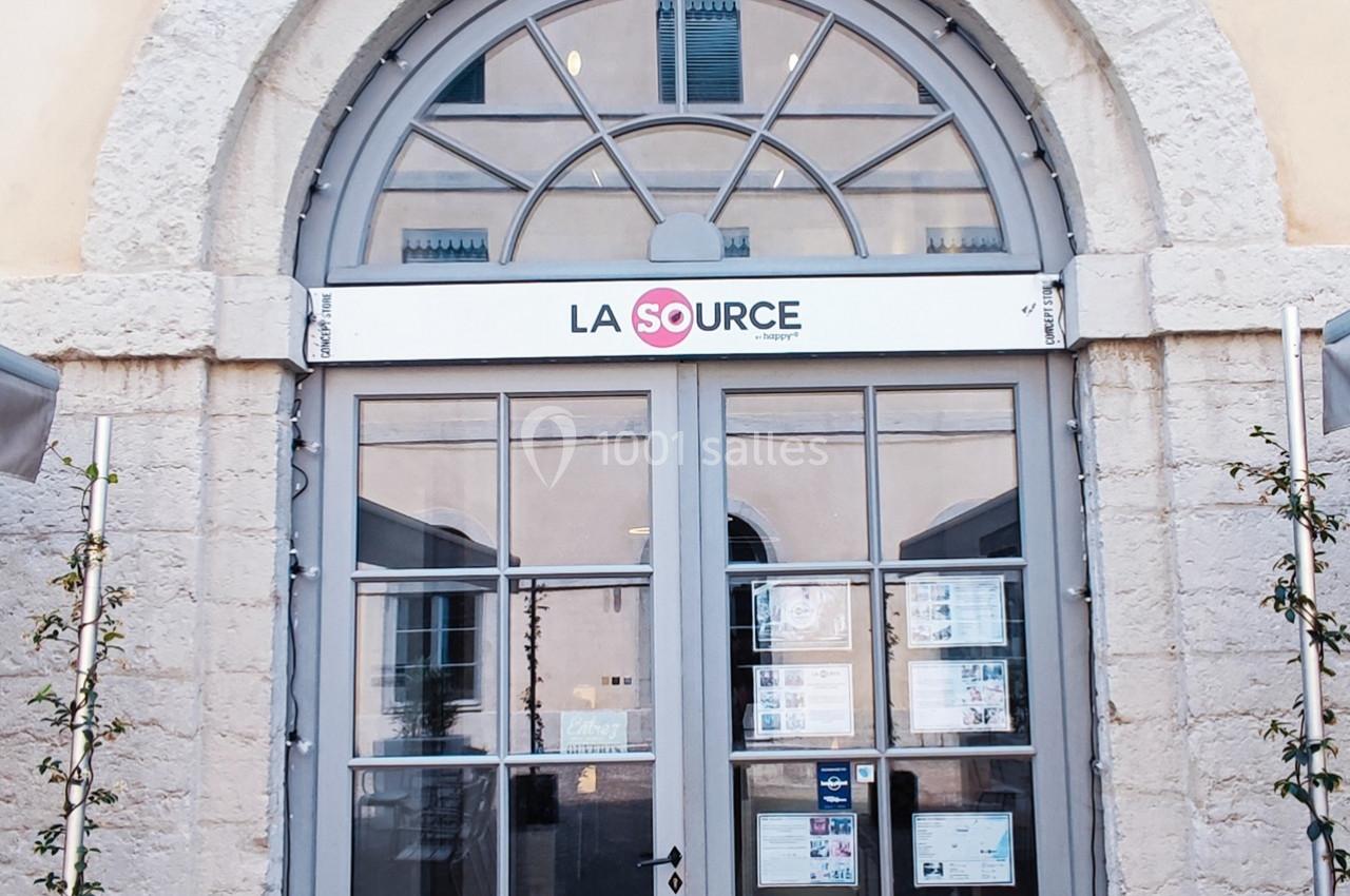 Façade d'un bâtiment avec une porte vitrée et une enseigne ’La Source’ surmontée d'une arche en pierre.