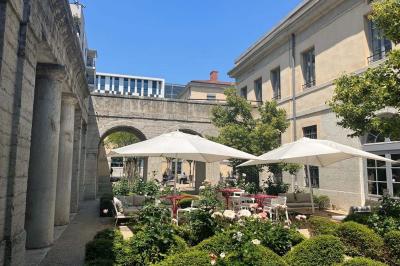 Groupe de personnes rassemblées autour de tables sous des parasols dans une cour extérieure avec végétation.