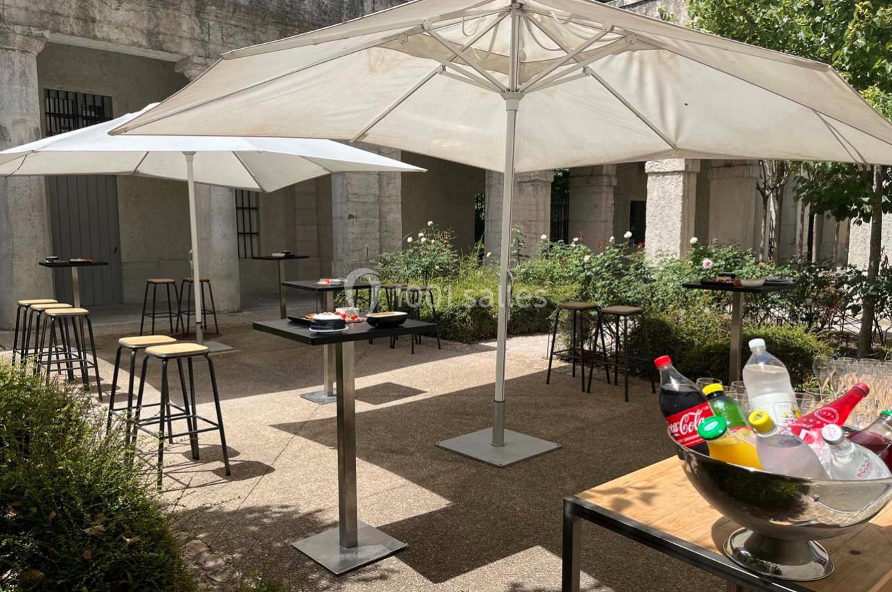 Terrasse extérieure avec tables hautes, chaises, parasols blancs et un seau rempli de boissons fraîches.