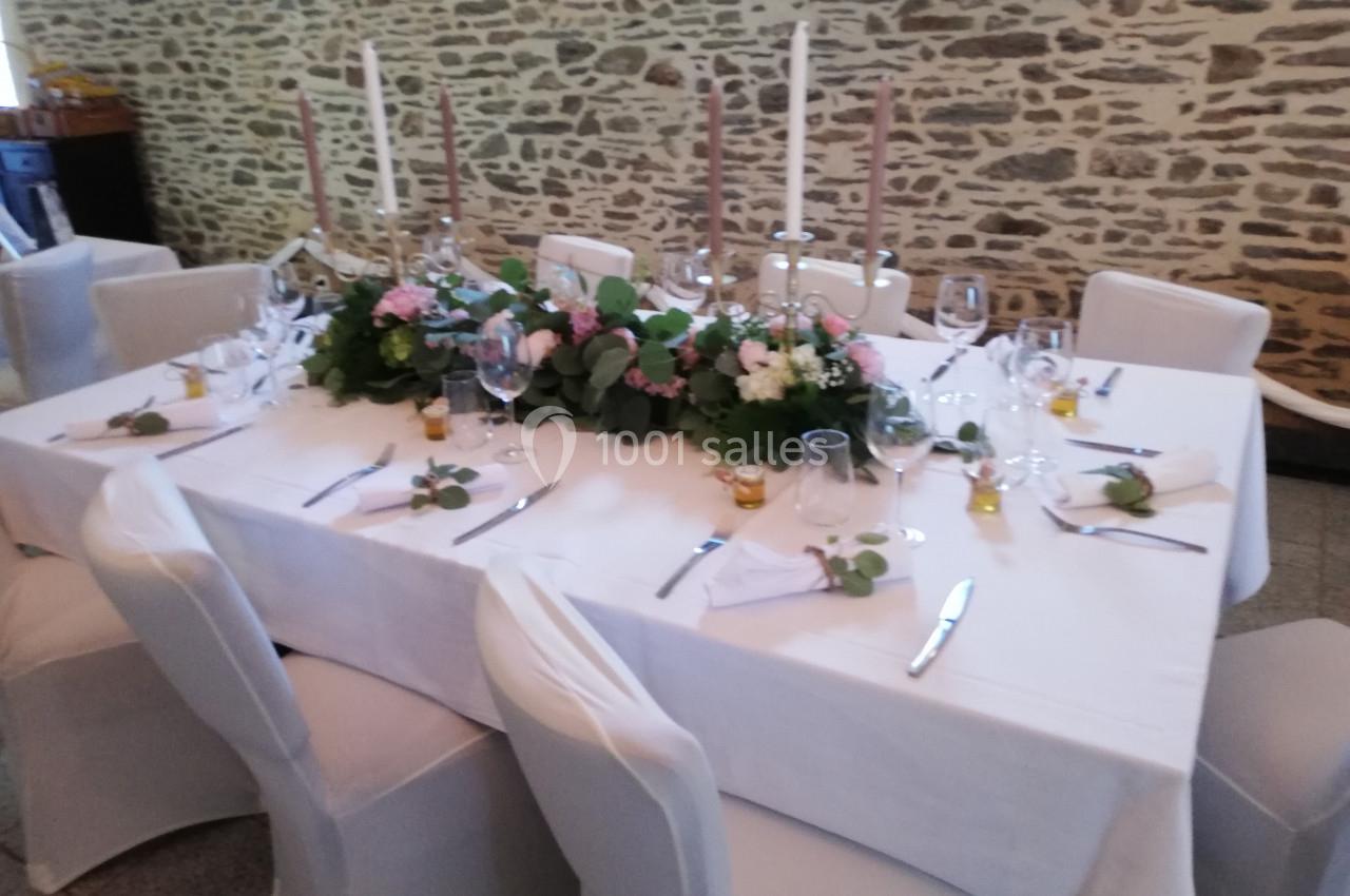 Table élégamment dressée avec nappes blanches, bougies, vaisselle et décoration florale dans une salle en pierre apparente.