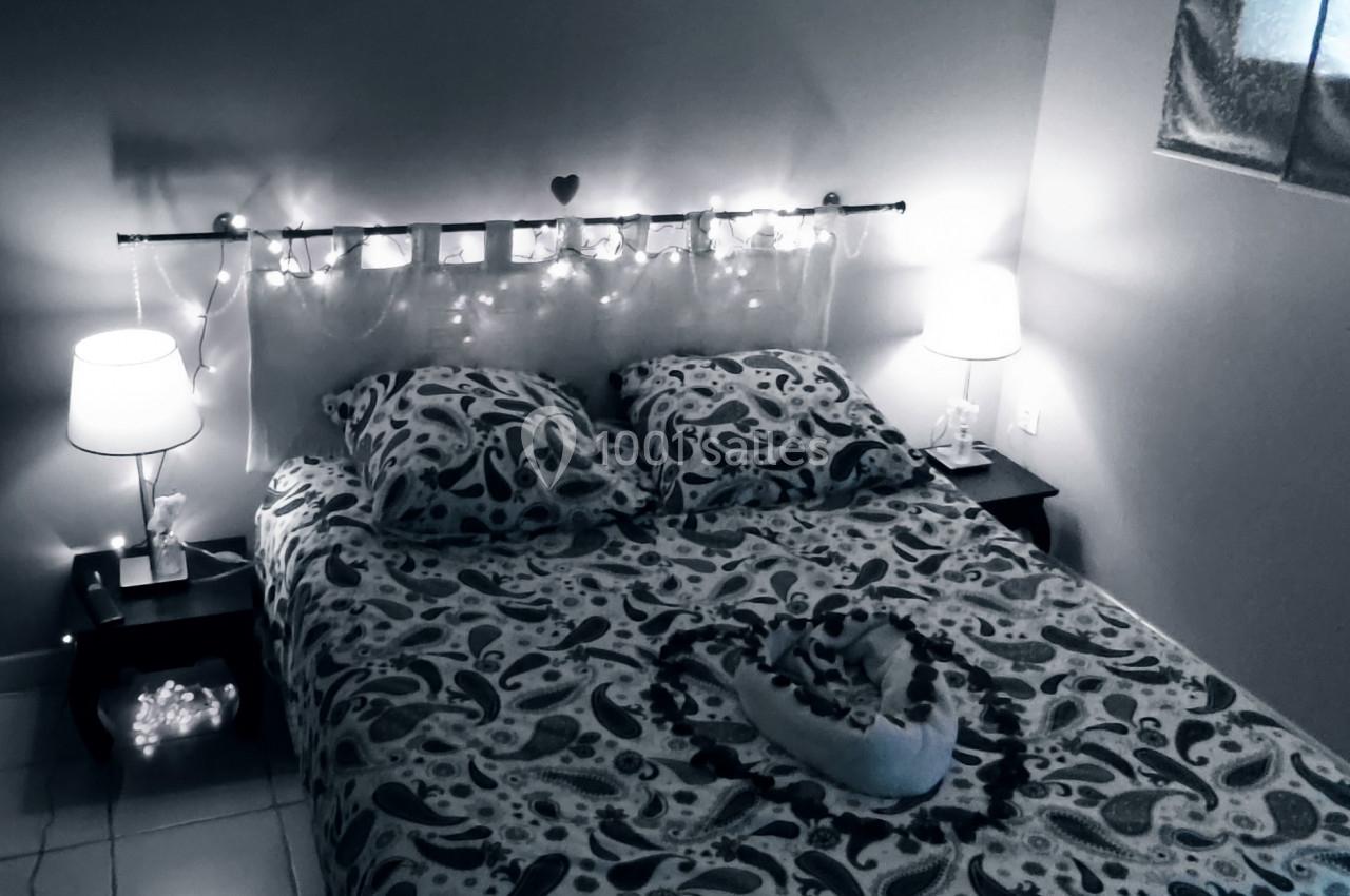 Lit double avec une parure à motifs, encadré de lampes de chevet et une guirlande lumineuse dans une chambre sombre.