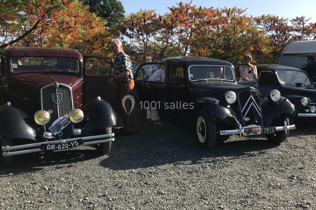 Trois voitures anciennes exposées en extérieur, avec des personnes observant ou interagissant avec les véhicules.