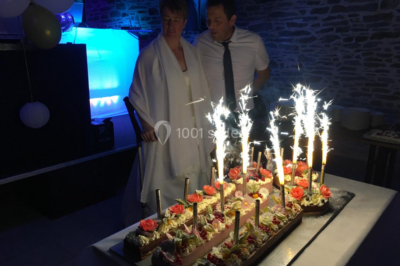 Un couple observe un gâteau décoré de bougies étincelantes lors d'une célébration dans une salle éclairée.