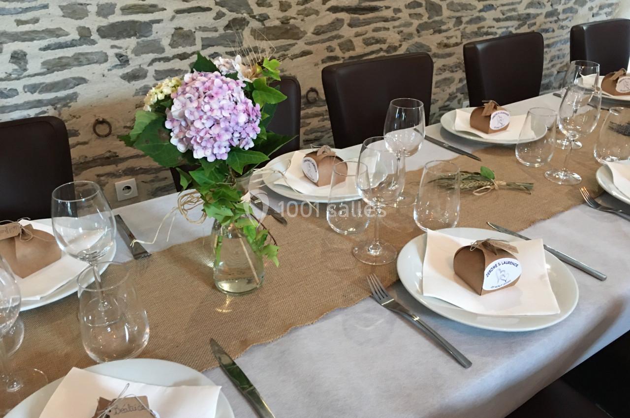 Table dressée avec une nappe en tissu, décorée de fleurs, vaisselle, verres et petits cadeaux emballés.