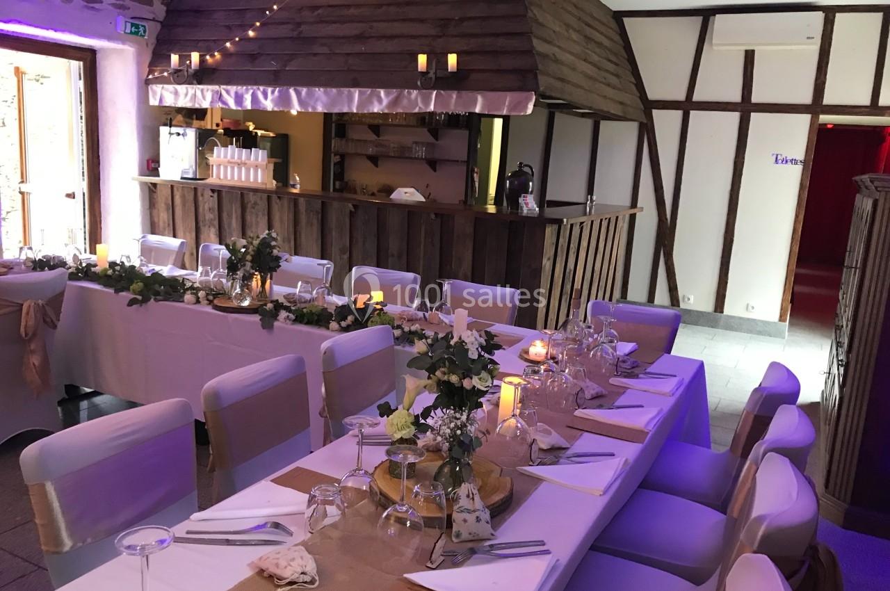 Salle de réception décorée avec des tables dressées, nappes blanches, chaises couvertes et guirlandes lumineuses.