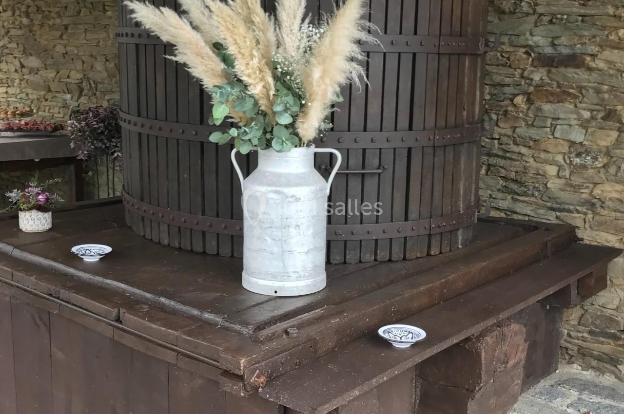 Presse à vin ancienne en bois avec un pot en métal contenant des herbes séchées, posée sur une structure rustique.