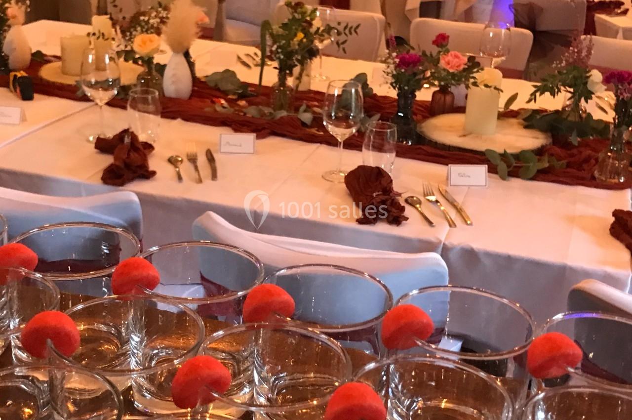 Tables décorées pour un événement avec nappes blanches, fleurs, bougies et verres garnis de fruits rouges.