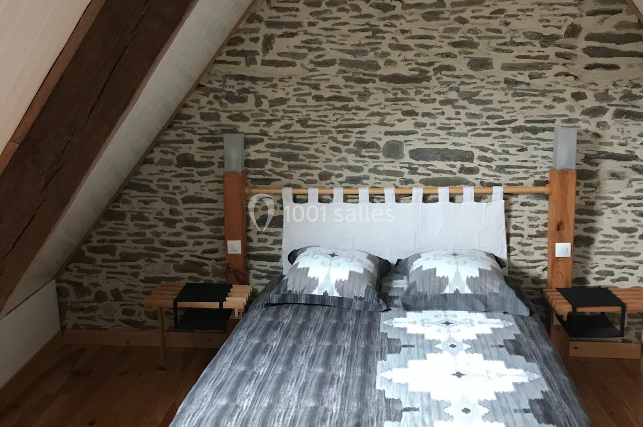 Chambre mansardée avec un lit double, mur en pierre apparente, poutres en bois et parquet au sol.