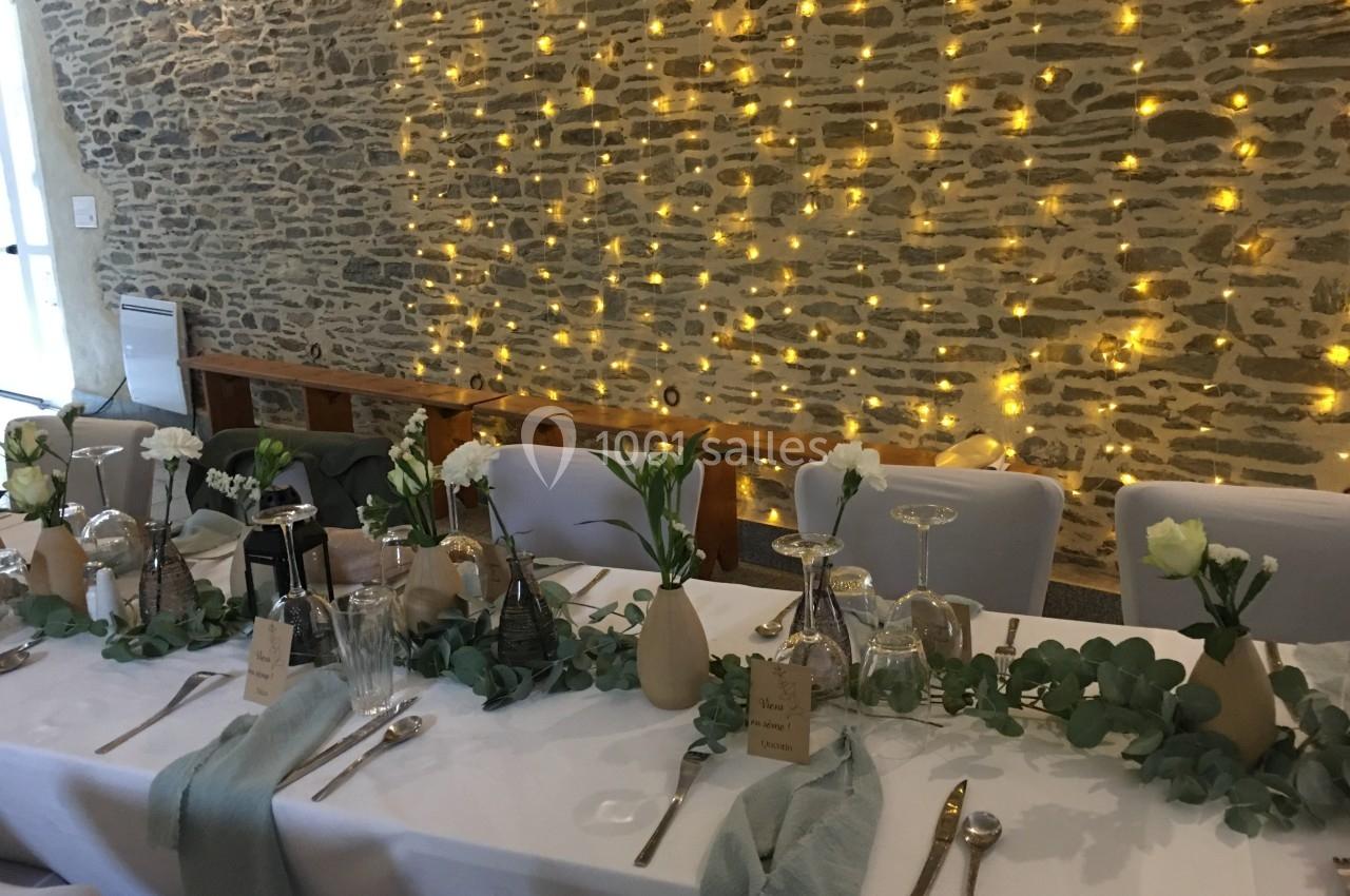 Table de réception décorée avec des fleurs blanches, des nappes blanches, des serviettes vertes et un mur en pierre illuminé.