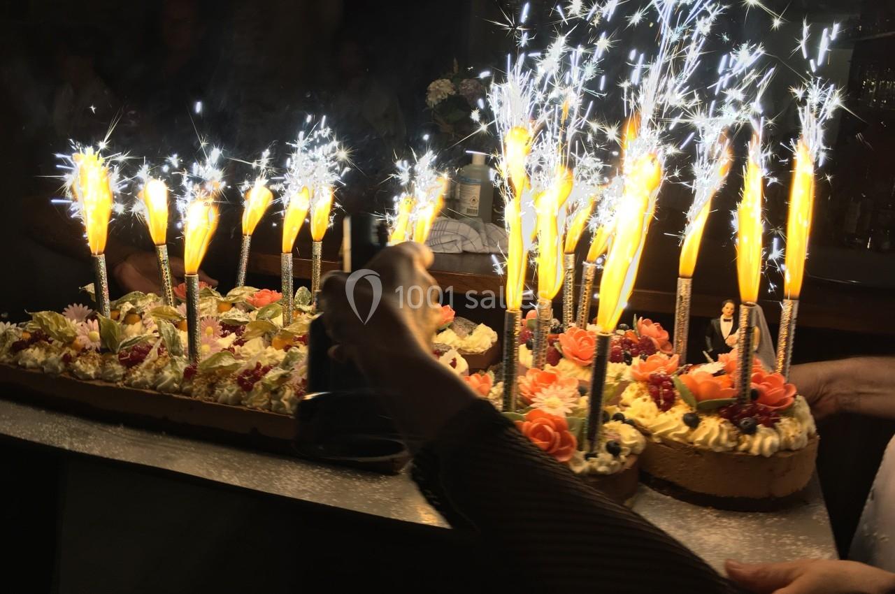 Gâteau décoré de fleurs en crème avec des bougies scintillantes allumées, tenu par une personne.